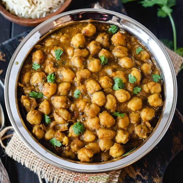 Close-up of a silver bowl filled with Chana Masala, garnished with fresh cilantro, with rice in the background.