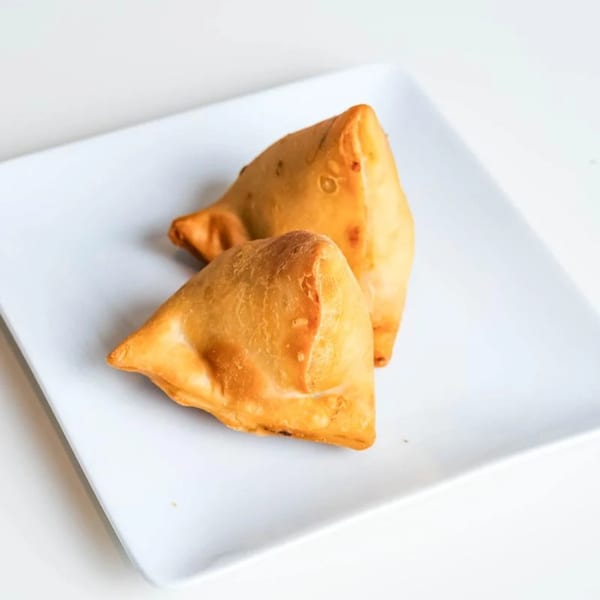 Two golden-brown samosas, a popular Indian pastry, rest on a white rectangular plate.