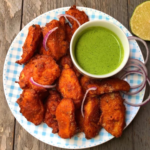 Bright orange Indian pakoras with red onion and green chutney on a blue and white checkered plate.