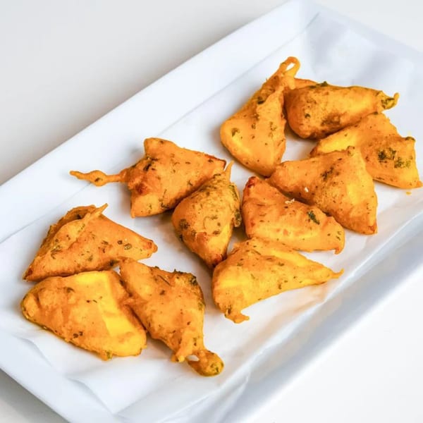 A white rectangular plate filled with golden-brown paneer pakora, a popular Indian appetizer.