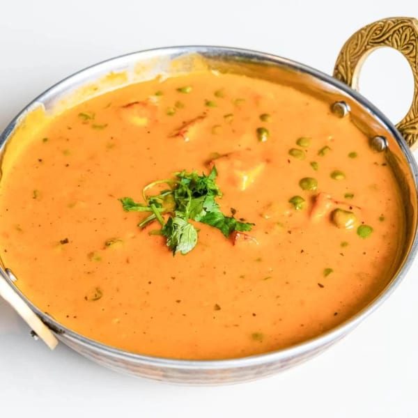 Indian curry with peas and paneer, garnished with cilantro, in a metal serving bowl.