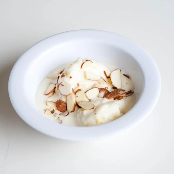 Kulfi, a traditional Indian ice cream, topped with sliced almonds in a white bowl.