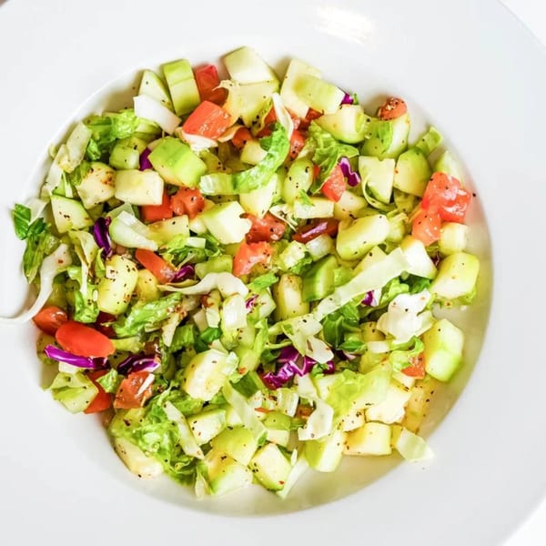 A vibrant Indian salad with diced cucumbers, tomatoes, and lettuce in a white bowl.