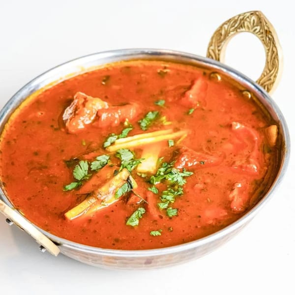 Indian curry in a metal bowl, garnished with fresh cilantro and ginger slivers.
