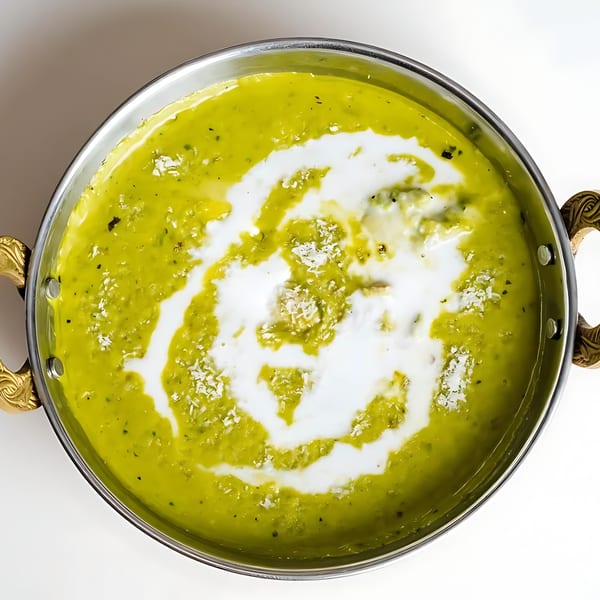 Vibrant green Indian curry with a swirl of white cream and shredded coconut in a metal pot.